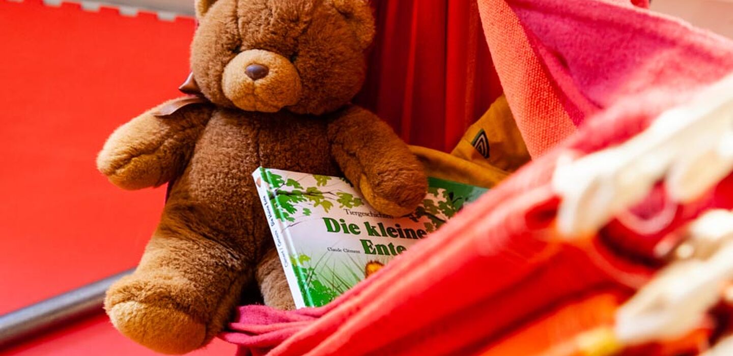 Ein Stoffbär in einer Hängematte. Beim Bären liegen noch Kinderbücher. 